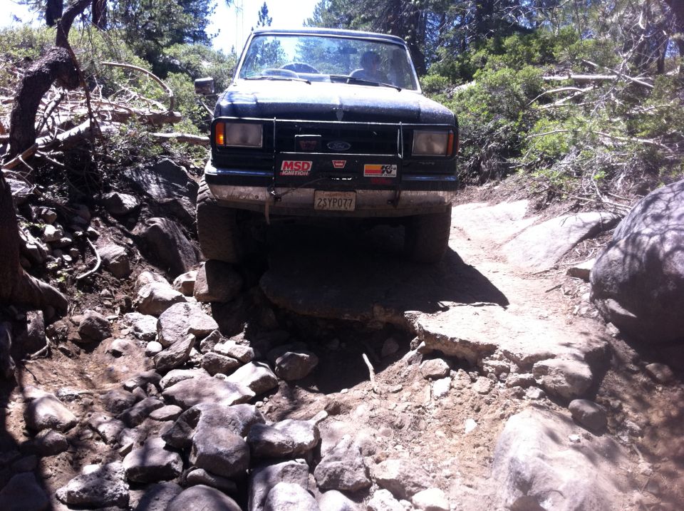 1990 Ford Bronco navigating a difficult rocky off-road path, front view
