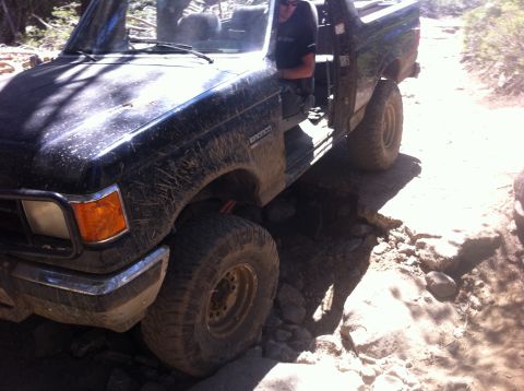 1990 Ford Bronco - A black Ford Bronco navigates a challenging rocky terrain on an off-road trail.