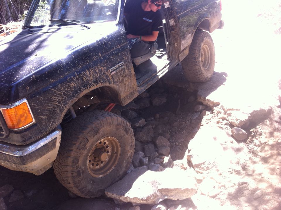 Black 1990 Ford Bronco with mud splatters navigating a rocky trail