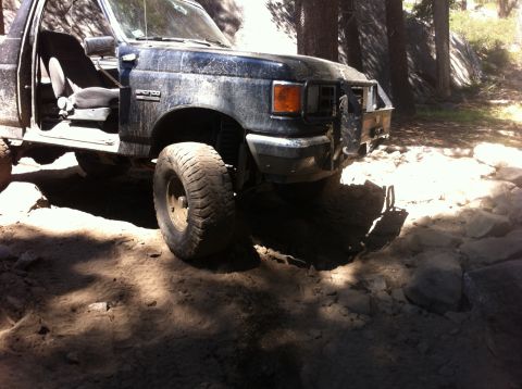 1990 Ford Bronco - This Ford Bronco is navigating a challenging, rocky off-road path in a wooded area.