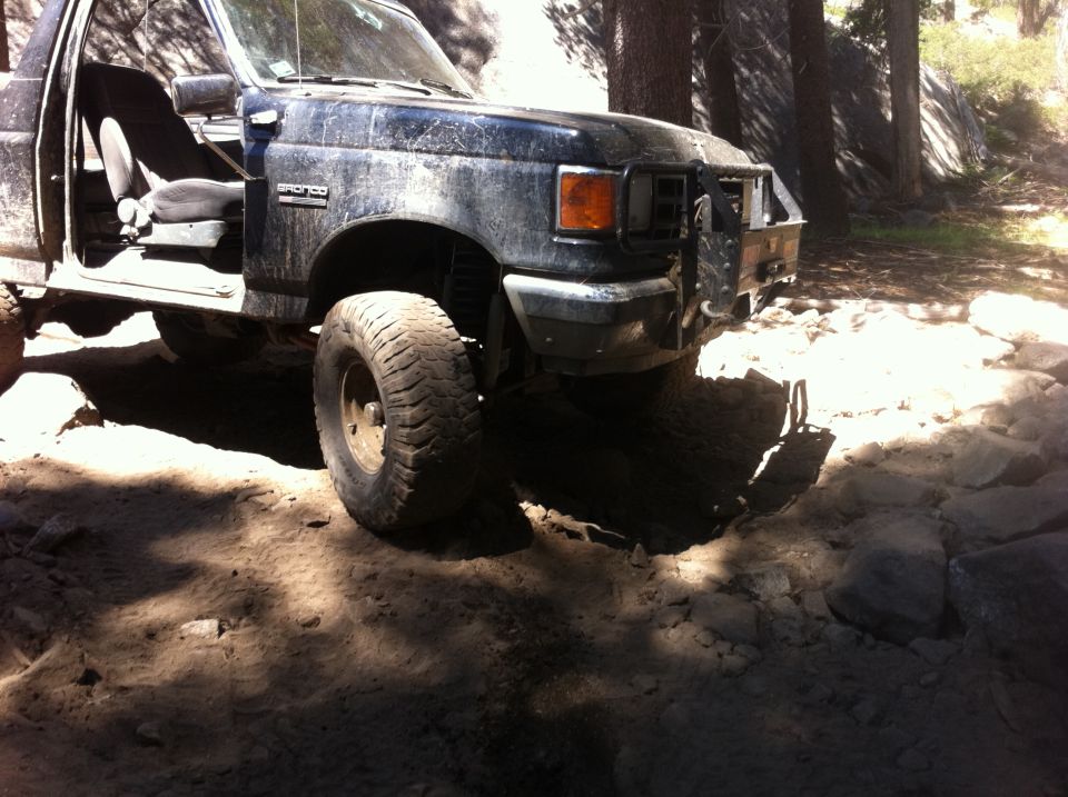 Muddy Ford Bronco with doors removed, driving on a rocky trail