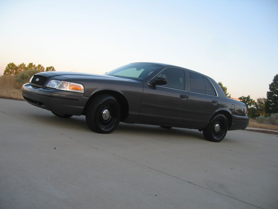 Dark gray sedan parked on concrete, front quarter view. Black wheels, tinted rear windows