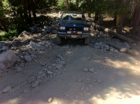 1990 Ford Bronco - A dark blue Ford Bronco navigates a challenging rocky terrain on an off-road trail.