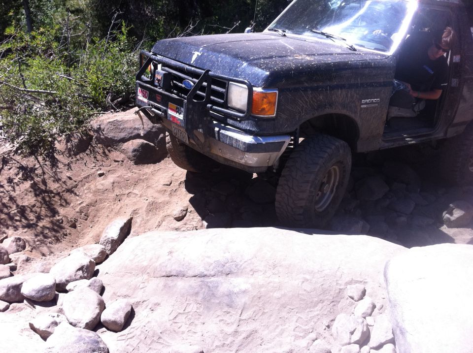 Black Ford Bronco navigating rocky terrain, front end angled up a dirt incline