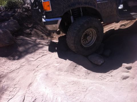 1990 Ford Bronco - A 1990 Ford Bronco navigates a challenging off-road course with large rocks and sandy soil.