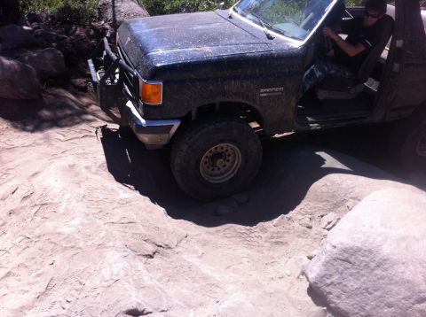 1990 Ford Bronco - A black Ford Bronco navigates a challenging rocky trail with its doors open.