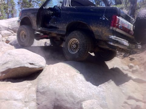 1990 Ford Bronco - A black Ford Bronco navigates a rocky trail, kicking up dust.