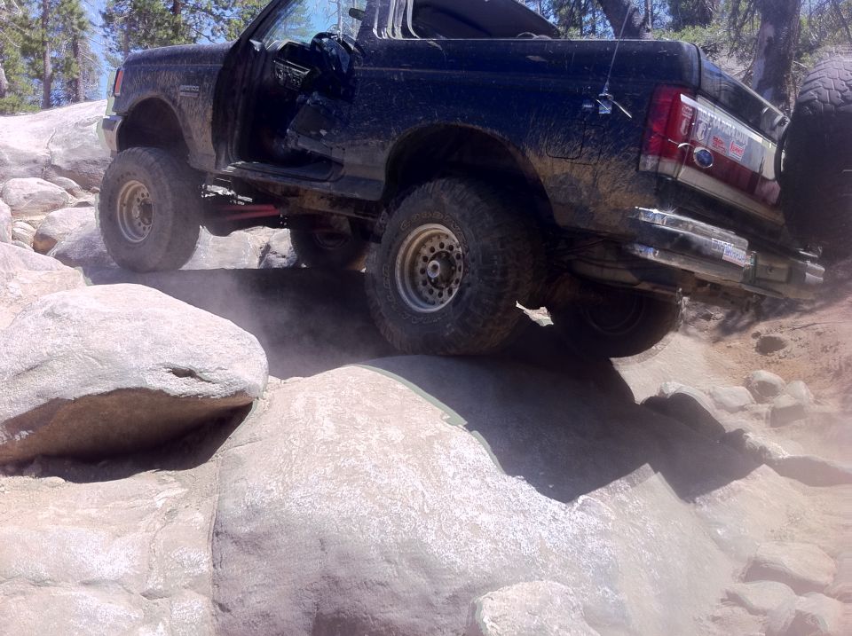 Black Ford Bronco with door open, driving over rocks