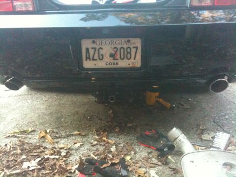 2008 Ford Mustang - The rear of a black car is shown with a Georgia license plate and exhaust pipes. Tools are scattered on the ground.