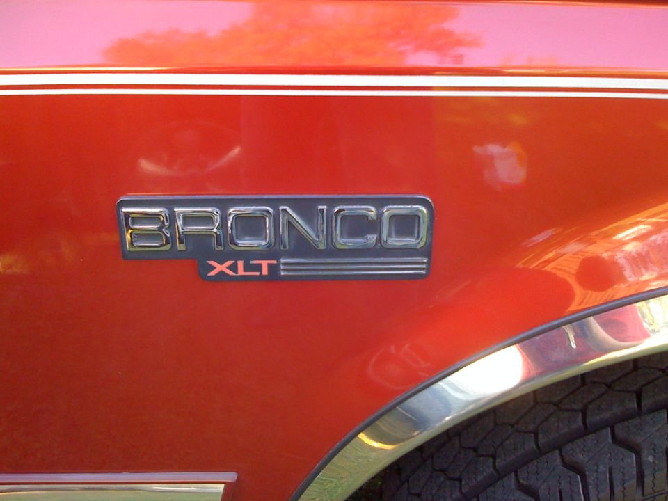 1996 Ford Bronco XLT emblem on red body panel with chrome trim and tire visible
