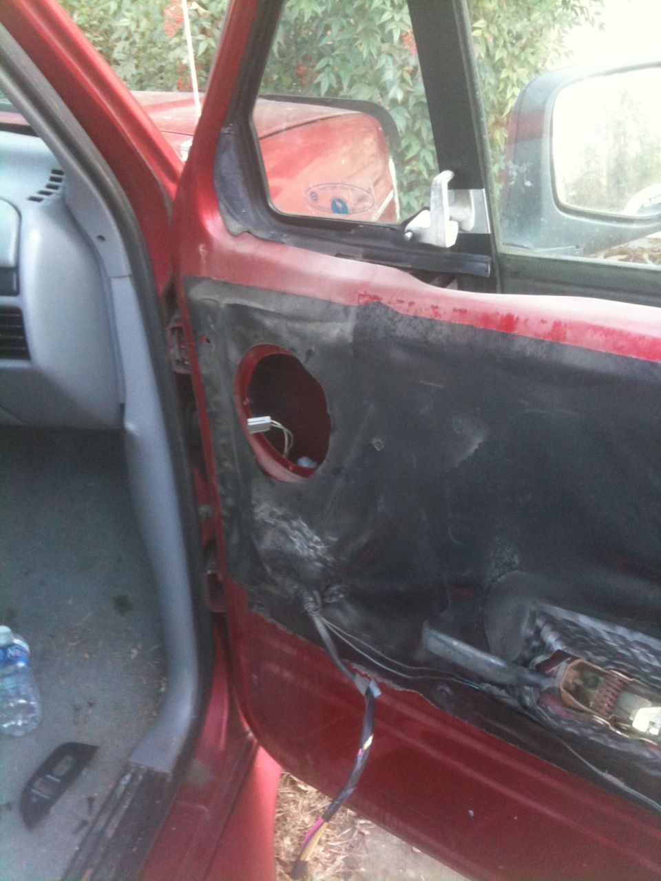 Red Bronco passenger door with panel removed, showing vapor barrier, empty speaker hole, and wiring.