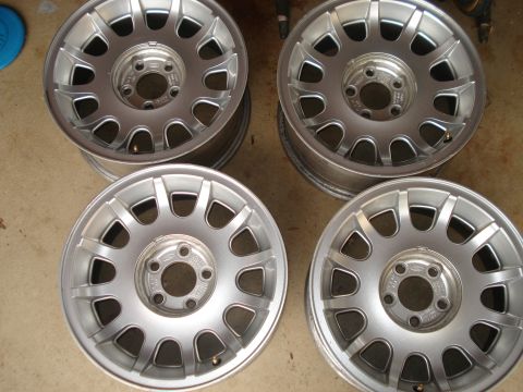 2000 Ford Crown Victoria - A set of four silver alloy wheels, likely for a Ford vehicle, are displayed on a concrete surface.