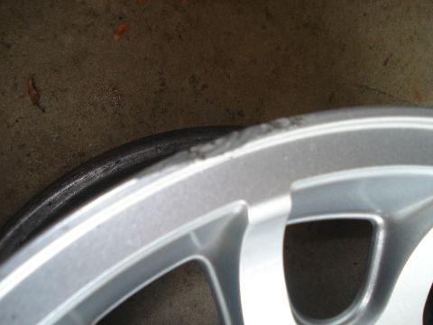 2000 Ford Crown Victoria - Close-up of a damaged silver alloy wheel rim with a tire edge visible.