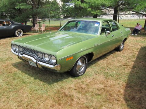 1991 Ford LTD Crown Victoria - green 1970s four-door sedan with quad headlights parked on grass at an outdoor car show, a person seated nearby.