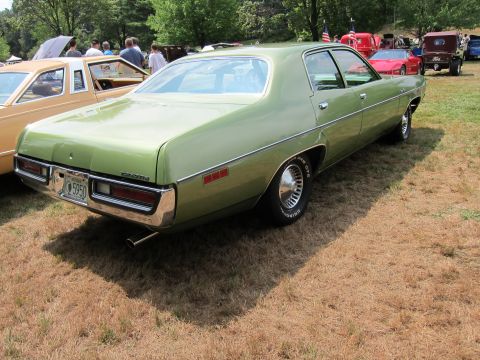 1991 Ford LTD Crown Victoria - Rear three-quarter view of a green 1970s four-door sedan on grass among other show cars and a US flag.