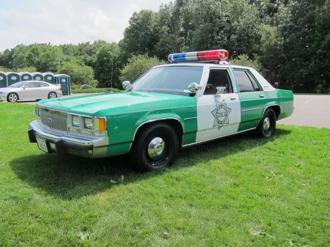 1991 Ford LTD Crown Victoria - green-and-white Ford LTD Crown Victoria police cruiser with roof light bar and a star emblem sits on a grassy field at a car show.