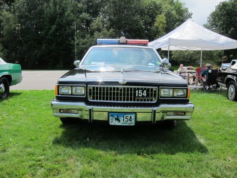 1991 Ford LTD Crown Victoria - Head-on view of a black-and-white Chevrolet police sedan numbered 154, showing grille, quad headlights and roof light bar.