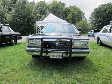 1991 Ford LTD Crown Victoria - Head-on view of a dark Ford police sedan with a chrome push bumper and California plate reading 888849 parked on grass.
