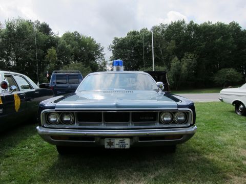 1991 Ford LTD Crown Victoria - Head-on view of a dark blue vintage Dodge police sedan with quad headlights, chrome grille and a single roof beacon on grass.