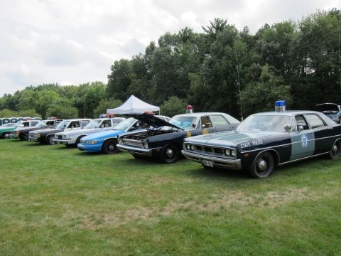 1991 Ford LTD Crown Victoria - long row of vintage state police cruisers parked on grass, led by a two-tone blue Dodge marked STATE POLICE.