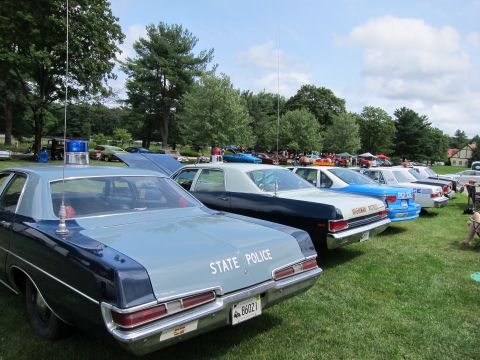 1991 Ford LTD Crown Victoria - Rear view of a row of vintage State Police sedans parked on grass, the nearest marked STATE POLICE with tall whip antenna.
