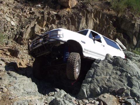 1993 Ford Bronco - This modified SUV navigates a challenging rocky terrain with its tires elevated.