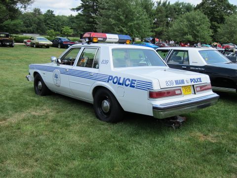 1991 Ford LTD Crown Victoria - White Miami Police sedan number 839 with blue striping, rear three-quarter view on a grass show field with other cars behind.