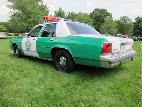 1991 Ford LTD Crown Victoria - Green-and-white Sheriff sedan with star emblem and light bar, rear three-quarter view parked on grass at a car show.