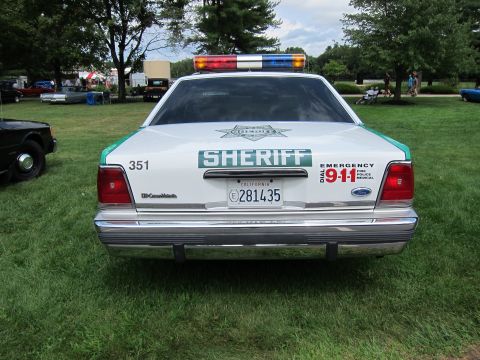 1991 Ford LTD Crown Victoria - Rear of a white Ford Sheriff sedan marked SHERIFF, EMERGENCY DIAL 9-1-1, with California plate, parked on grass.