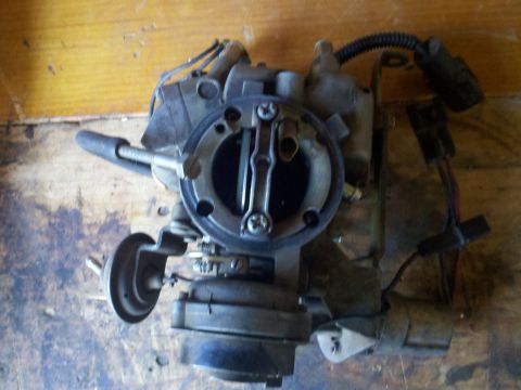 1986 Ford Bronco - A carburetor, likely from an older vehicle, is shown close-up against a wooden background.