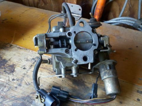 1986 Ford Bronco - A carburetor assembly, likely for a Ford vehicle, is shown resting on a wooden surface.