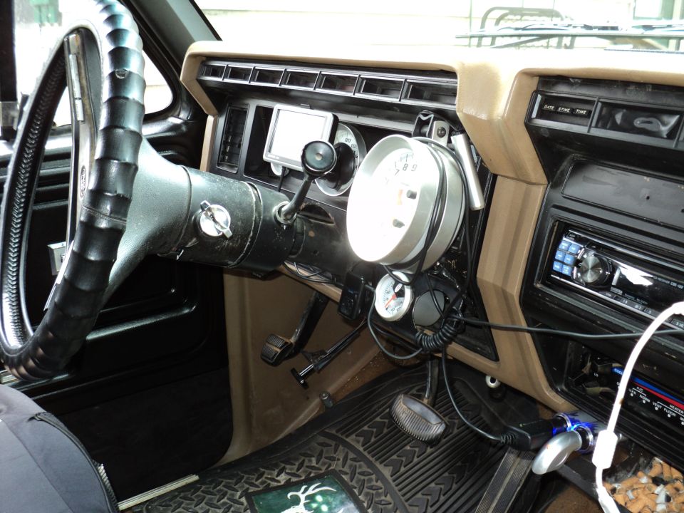 Interior shot of a truck's dashboard, showing a large steering wheel, aftermarket gauges, and a GPS unit