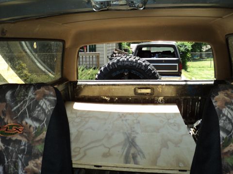1986 Ford Bronco - A dark Ford Bronco is visible through the rear window of another vehicle, with a spare tire mounted inside.