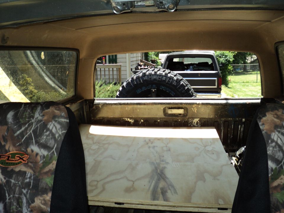 Rear view of a dark-colored Ford Bronco with a spare tire mounted inside, seen through a window