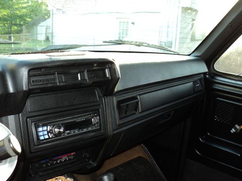1986 Ford Bronco - The dashboard of a vehicle, an aftermarket stereo system and air vents, with a view of the exterior through the windshield.