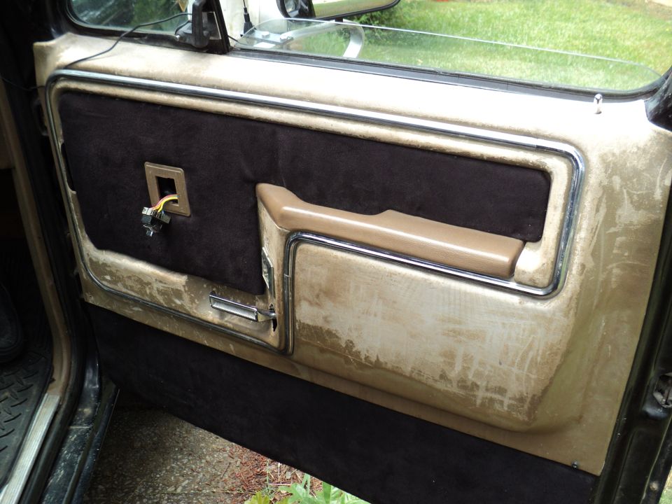 Interior door panel with brown fabric and tan trim. Window crank and door handle visible