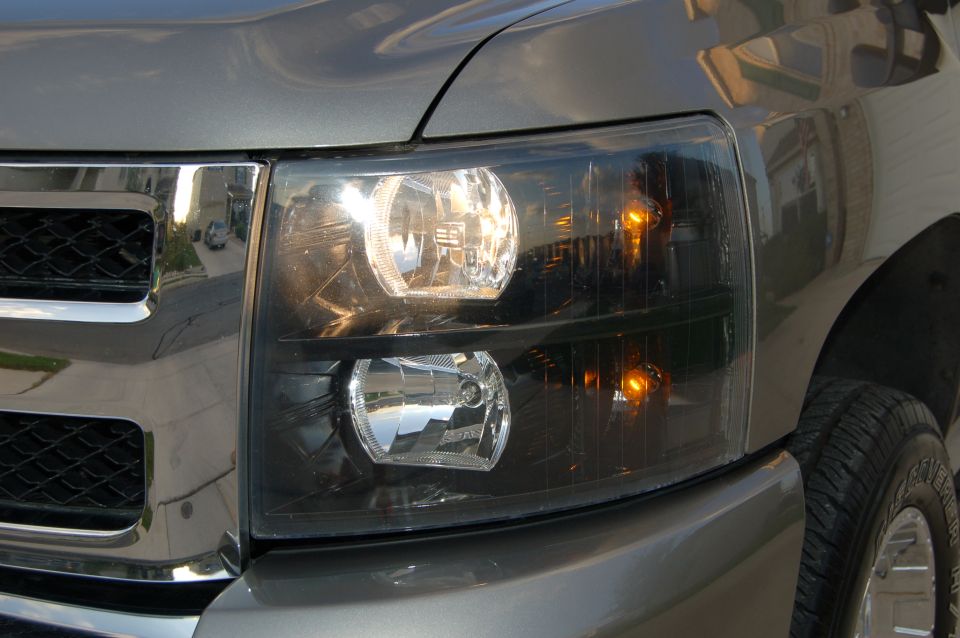Gray truck's front headlight assembly with chrome grille detail. Headlights are on