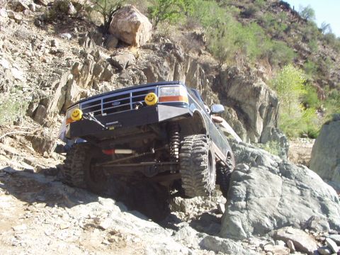1993 Ford Bronco - This 1993 Ford Bronco is shown tackling a challenging off-road course with significant rock obstacles.