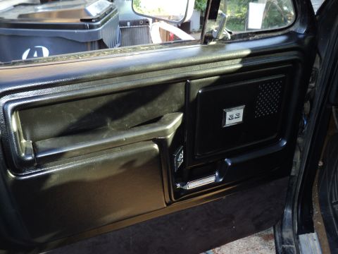 1986 Ford Bronco - Close-up of a vehicle's interior door panel, showing the handle, armrest, and a small badge.