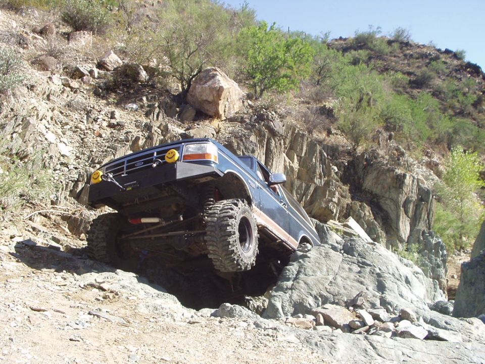 Ford Bronco climbing rocks on a trail. Has smiley face stickers on the headlights