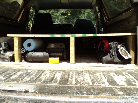 1986 Ford Bronco - The cargo area of a vehicle is organized with a wooden shelf holding various tools and supplies.