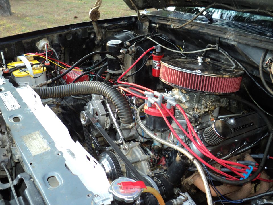 Engine bay with V8 engine, red spark plug wires, and air filter. Some text visible on valve cover
