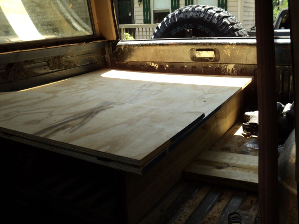 Plywood platform built inside the bed of a truck, with a spare tire visible in the background