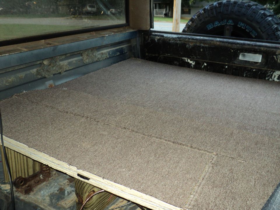 Carpeted truck bed interior with a spare tire visible in the background