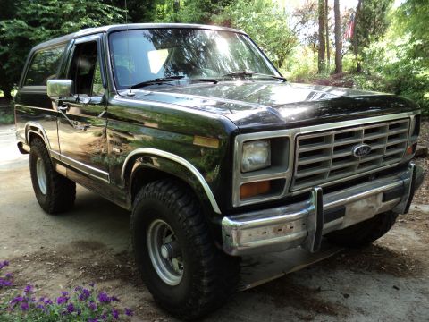 1986 Ford Bronco - This black Ford Bronco is shown from a three-quarter front view, parked outdoors.