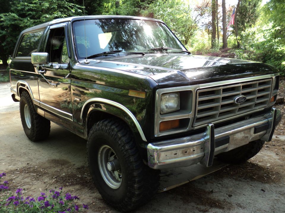 Black Ford Bronco parked on a dirt driveway with trees in the background