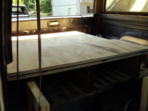 1986 Ford Bronco - Plywood sheets are loaded into the bed of a pickup truck, with another vehicle visible outside.