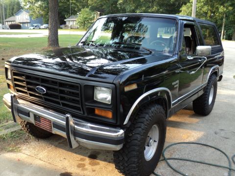 1986 Ford Bronco - A black Ford Bronco is shown from a three-quarter front angle, parked outdoors on a sunny day.