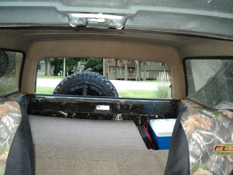 1986 Ford Bronco - The interior of the vehicle shows camouflage seat covers and a spare tire mounted in the cargo area.