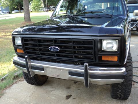 1986 Ford Bronco - Front view of a black Ford Bronco with a prominent grille and chrome bumper, showing off its lifted suspension.